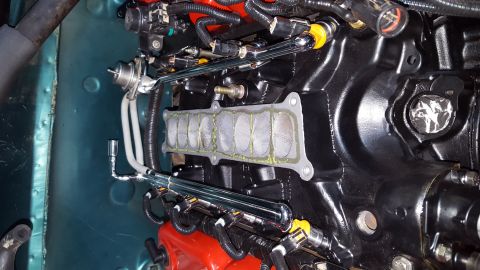 1996 Ford Bronco - A close-up view of a black engine intake manifold with a gasket and fuel rails installed. Chrome fuel lines run along the top of the manifo…