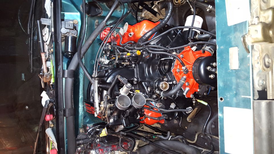 Black and orange engine with hoses and wiring in an engine bay.