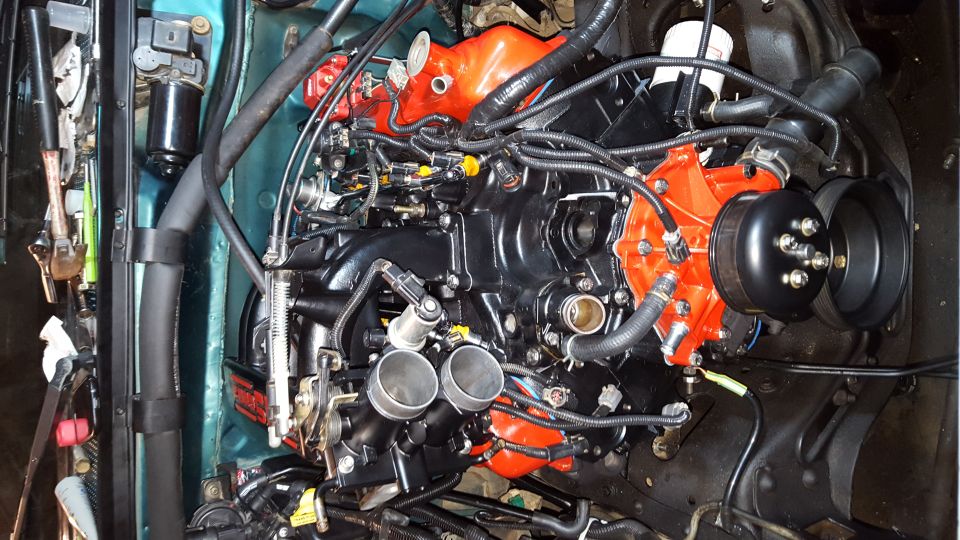 Rebuilt engine with black intake and orange valve covers, showing wires and hoses.