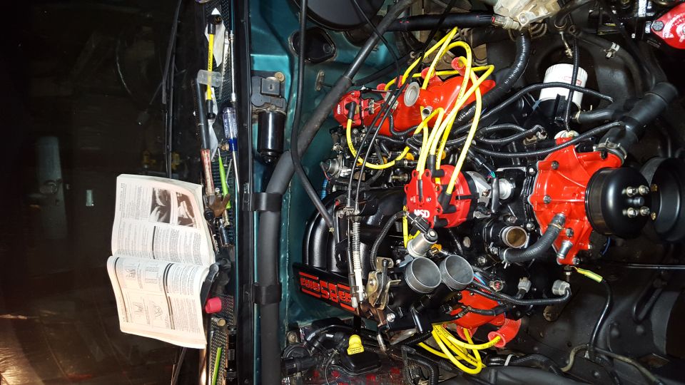 Modified engine bay with red MSD ignition, yellow wires, and open manual.