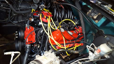 1996 Ford Bronco - A close-up view of a modified V8 engine bay, featuring a black intake manifold, red valve covers, and bright yellow spark plug wires. The e…
