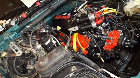 1996 Ford Bronco - A detailed view of a modified engine bay, likely from a 1990s Ford Bronco, featuring a black intake manifold with red lettering, bright red…