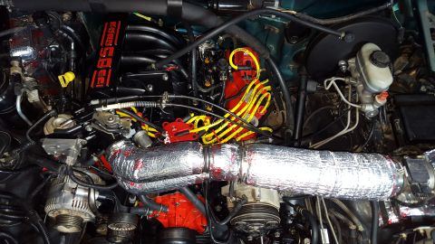 1996 Ford Bronco - A detailed, top-down view of a modified engine bay, featuring a black intake manifold with red "Ford Racing" text, yellow spark plug wires,…