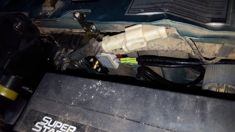 1996 Ford Bronco - A close-up view of wiring harness connections and a portion of a black battery case in a vehicle's engine bay. The wiring includes a white…