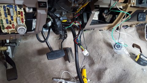 1996 Ford Bronco - Under the dashboard of a 1996 Ford Bronco, a variety of wires are exposed near the fuse box and pedals. A yellow utility knife and a measur…