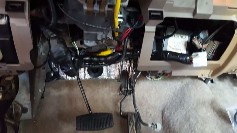 Vehicle dashboard interior with exposed wires, pedals, and sound deadening material.