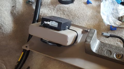 1996 Ford Bronco - A black electronic module with white connectors is mounted on a tan plastic trim piece inside a vehicle. The trim piece is attached to a te…