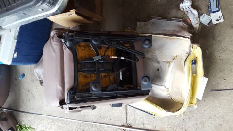 1996 Ford Bronco - A disassembled car seat with its metal frame exposed and the tan upholstery partially removed, revealing yellow foam padding. Tools and deb…