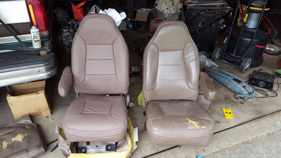 Two tan leather car seats, one worn, one new, in a garage.