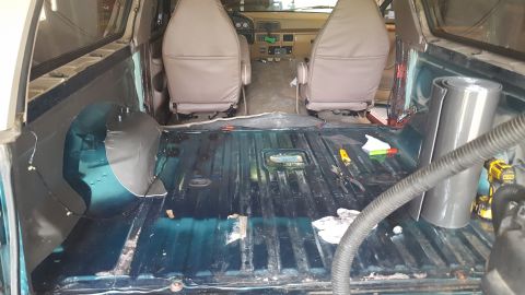 1996 Ford Bronco - The interior of a disassembled vehicle, likely a Ford Bronco, shows the floor stripped down to the metal, with insulation material being ap…