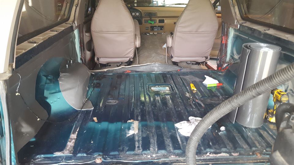 Interior of a disassembled Ford Bronco showing stripped floor, insulation, seats, and dashboard.