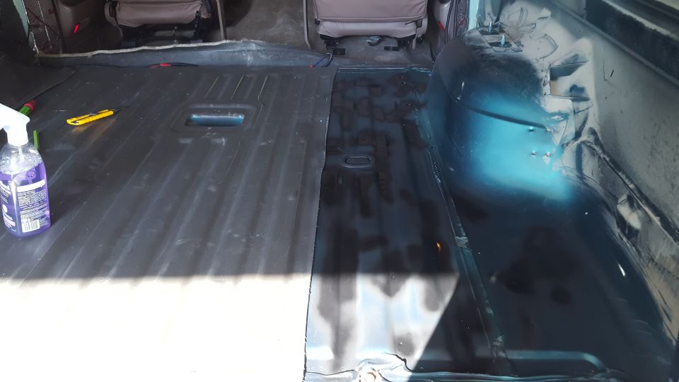 Interior of a vehicle showing the floor with sound deadening material, a spray bottle, and a utility knife.