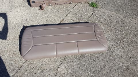 1996 Ford Bronco - A tan leather seat cushion is shown lying on a cracked concrete surface. Another part of a tan vehicle interior is visible in the upper por…