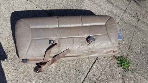 1996 Ford Bronco - A tan leather rear car seat with two seatbelt buckles is lying on a concrete surface. The seat appears to be from an older SUV or truck.