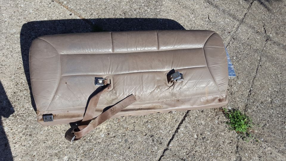 Tan leather rear car seat with seatbelt buckles on concrete
