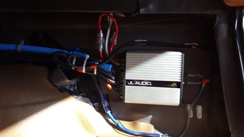 1996 Ford Bronco - A JL Audio amplifier is mounted inside a vehicle, with various wires and a blue conduit running nearby. The amplifier is silver with black…
