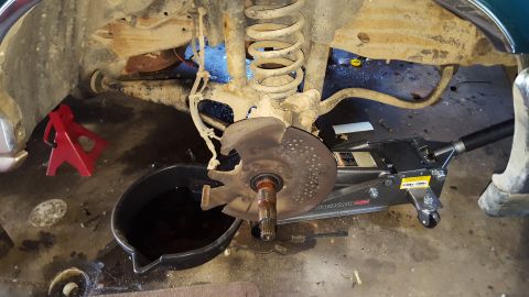 1996 Ford Bronco - A car's front suspension and brake rotor assembly are visible, supported by a red jack stand and a hydraulic floor jack. A drain pan filled…