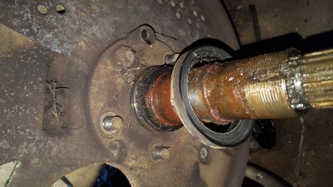 1996 Ford Bronco - A close-up view shows a heavily greased and splined axle shaft protruding from a rusty hub assembly, with a damaged seal visible.