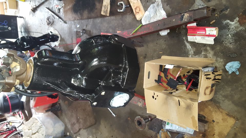 Black painted differential housing in a workshop with a box of parts.