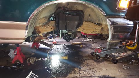 1996 Ford Bronco - The underside of a dark green vehicle, likely a 1996 Ford Bronco, is shown lifted on jack stands in a garage. The rear axle and differentia…