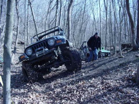 1992 Ford Bronco - A Jeep Wrangler navigates a muddy, wooded trail with another vehicle visible in the background.