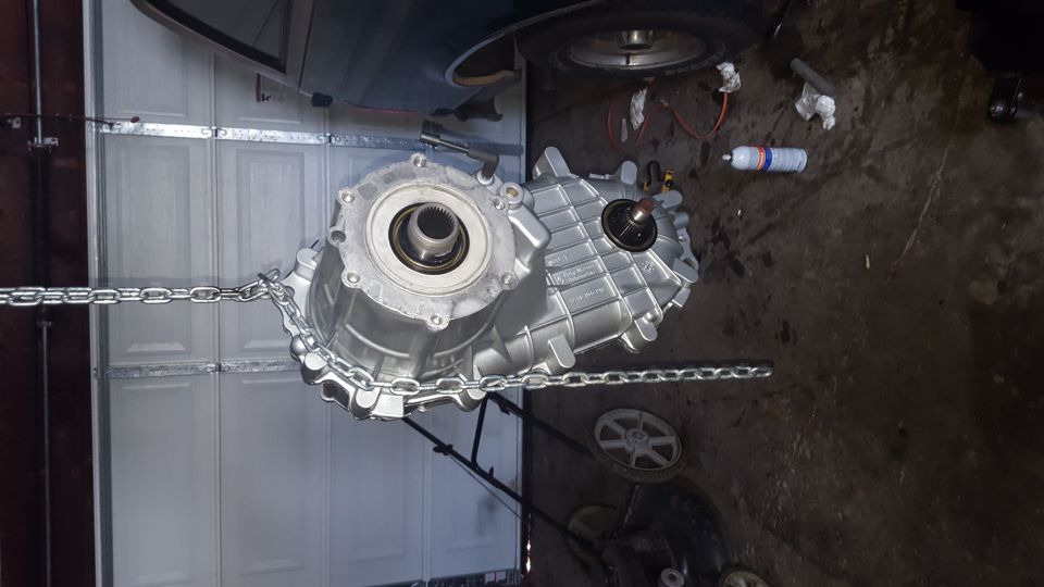 Silver transfer case suspended by chains in a garage.