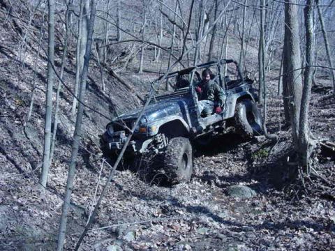 1992 Ford Bronco - A driver navigates a challenging off-road trail in a Jeep Wrangler, surrounded by trees and fallen leaves.