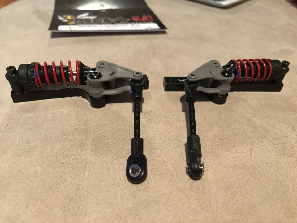 Two RC car shock assemblies with red springs and gray mounts.