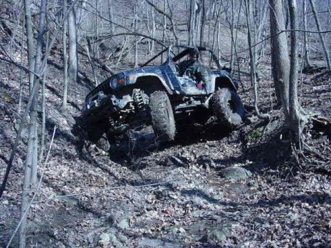 1992 Ford Bronco - An off-road vehicle navigates a steep, muddy incline in a dense forest.