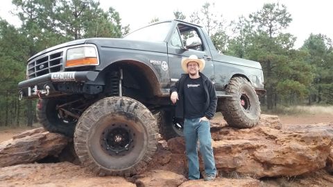 1995 Ford Bronco - A man in a cowboy hat stands next to a lifted, dark gray 1995 Ford Bronco with large off-road tires, positioned on large rocks.