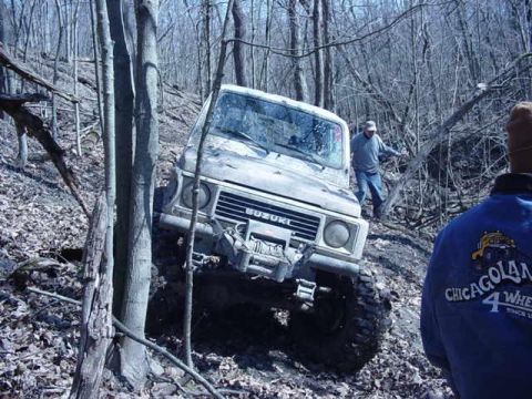 1992 Ford Bronco - A Suzuki Samurai navigates a challenging wooded terrain, equipped with a front winch for off-road recovery.