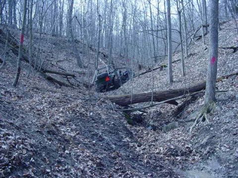 1992 Ford Bronco - Off-road vehicle stuck on a steep, muddy, wooded hillside.