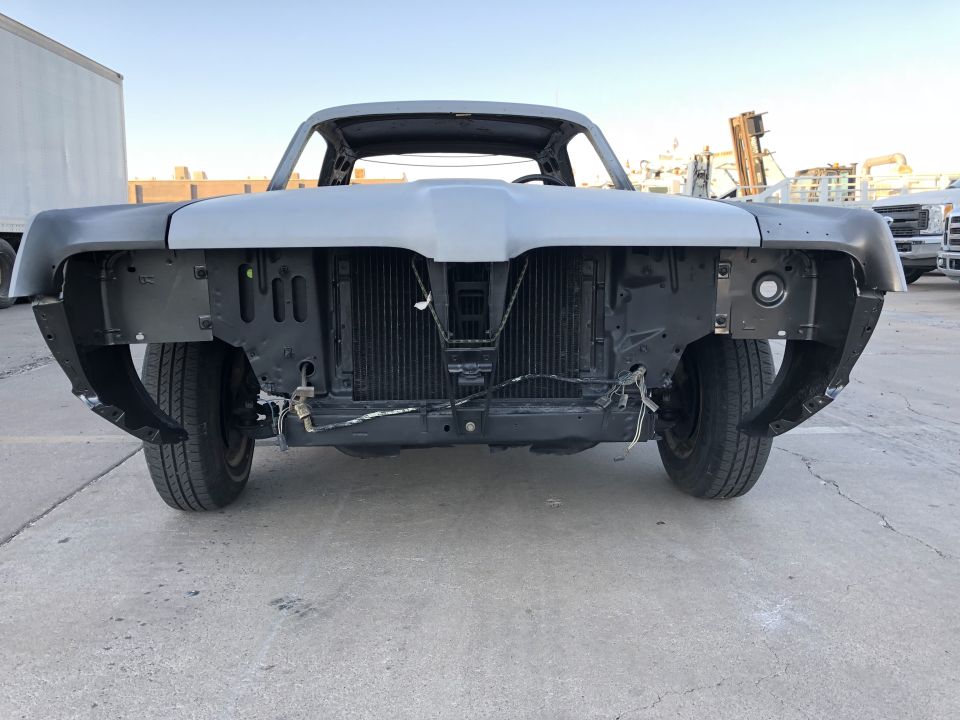 Classic car front end with hood and fenders removed, showing radiator and engine bay.