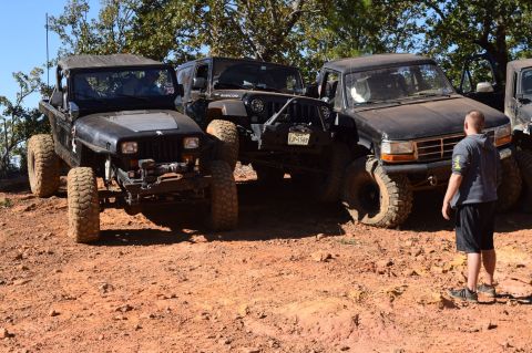 1995 Ford Bronco - A black 1995 Ford Bronco is parked on a dirt trail next to two black Jeep Wranglers. A man stands to the right of the Bronco, facing away f…