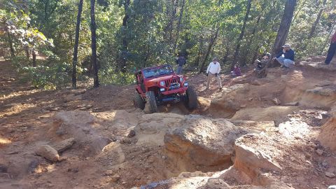 1995 Ford Bronco - A red Jeep Wrangler is navigating a rocky, off-road trail with several spectators watching from the side. The vehicle is angled upwards, wi…