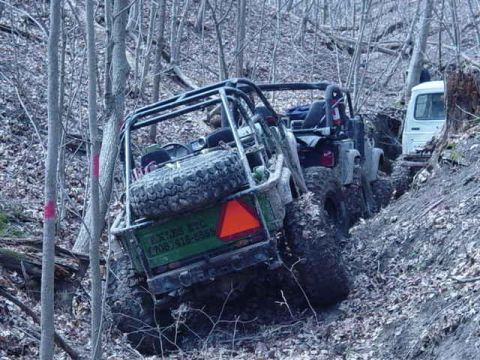 1992 Ford Bronco - Off-road vehicles navigate a challenging, muddy incline in a dense forest.
