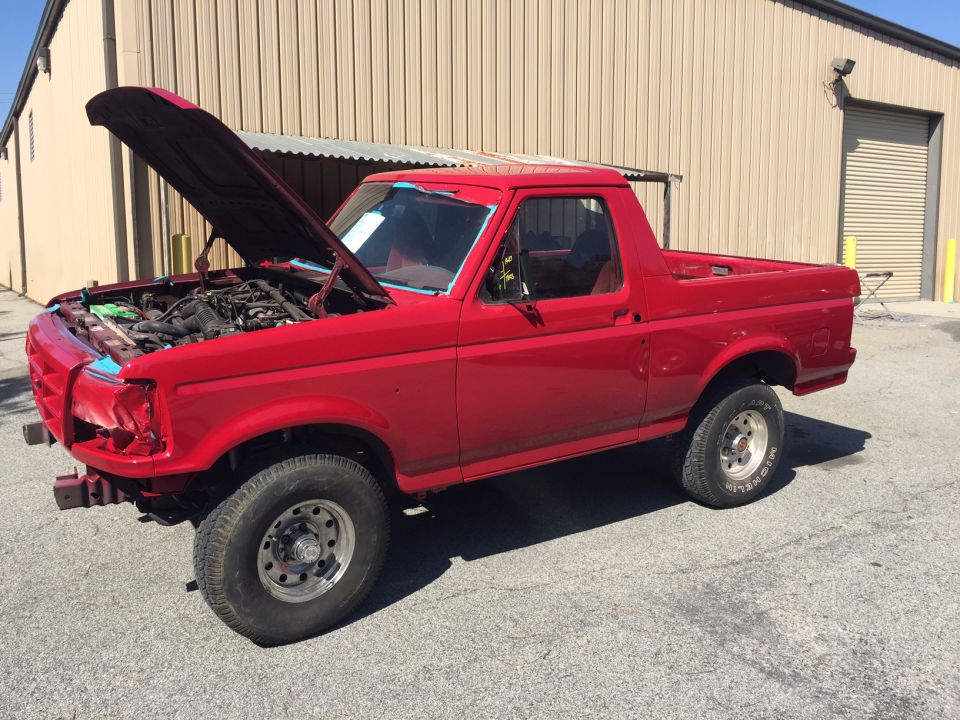 Red Ford Bronco with hood open, parked outside a building.