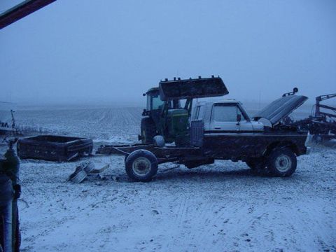 1992 Ford Bronco - A truck chassis sits in the snow with a tractor loader behind it, under a cloudy sky.