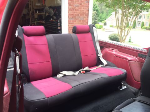 1994 Ford Bronco - The interior of a red Ford Bronco shows a rear bench seat with pink and gray seat covers. The seat has two headrests and a gray seatbelt is…