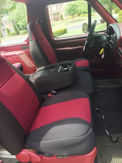 1994 Ford Bronco - The interior of a red and black 1994 Ford Bronco shows the front seats and center console with cup holders. The view is from the passenger…