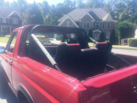 1994 Ford Bronco - The rear passenger side of a red Ford Bronco is shown with the top removed, revealing the interior seats and a roll bar. The vehicle is par…