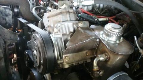 1995 Ford Bronco - A close-up view of a modified engine bay, focusing on the air conditioning compressor and a custom-mounted reservoir with a silver cap. The…