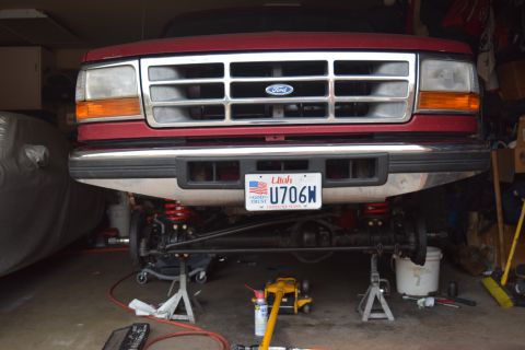 1995 Ford Bronco - The front of a red Ford Bronco is raised on jack stands in a garage, showing its suspension and undercarriage. A Utah license plate reading…