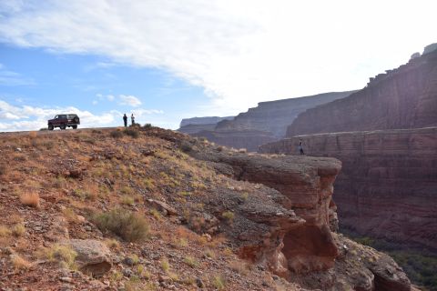 1995 Ford Bronco - A maroon 1995 Ford Bronco is parked on a rocky overlook, with two people standing nearby and a vast canyon stretching into the distance.