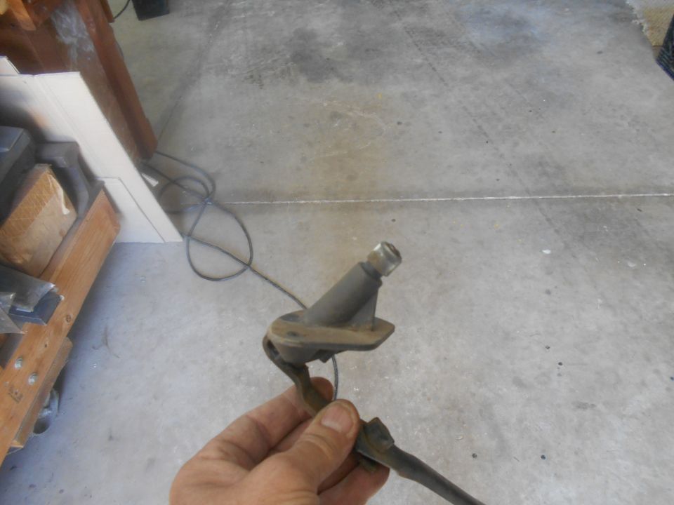 Close-up of a hand holding a metal vehicle part with a cable attached.