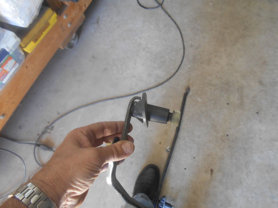 Hand holding a black clutch pedal assembly with a cable on concrete floor