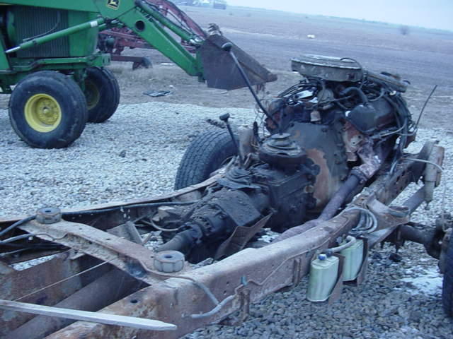 rusted vehicle chassis with engine and transmission, green tractor in background