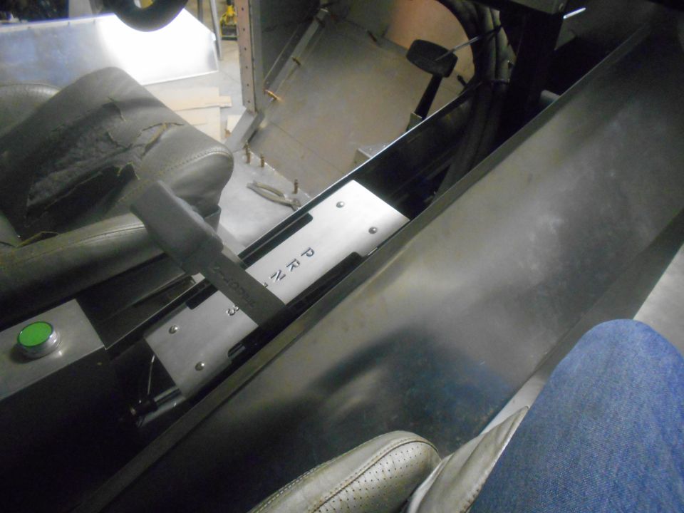 Vehicle interior center console with gear shifter, PRND markings, and green button. Worn driver's seat visible.