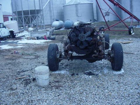1992 Ford Bronco - The engine and chassis of a truck are displayed outdoors, with farm structures in the background.