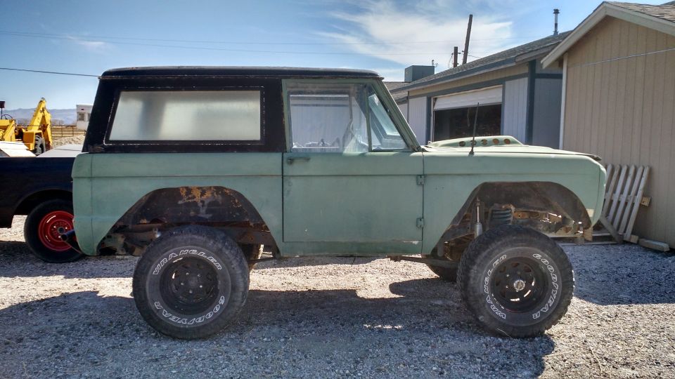 Side view of a vintage light green Ford Bronco with a black hardtop, undergoing restoration.